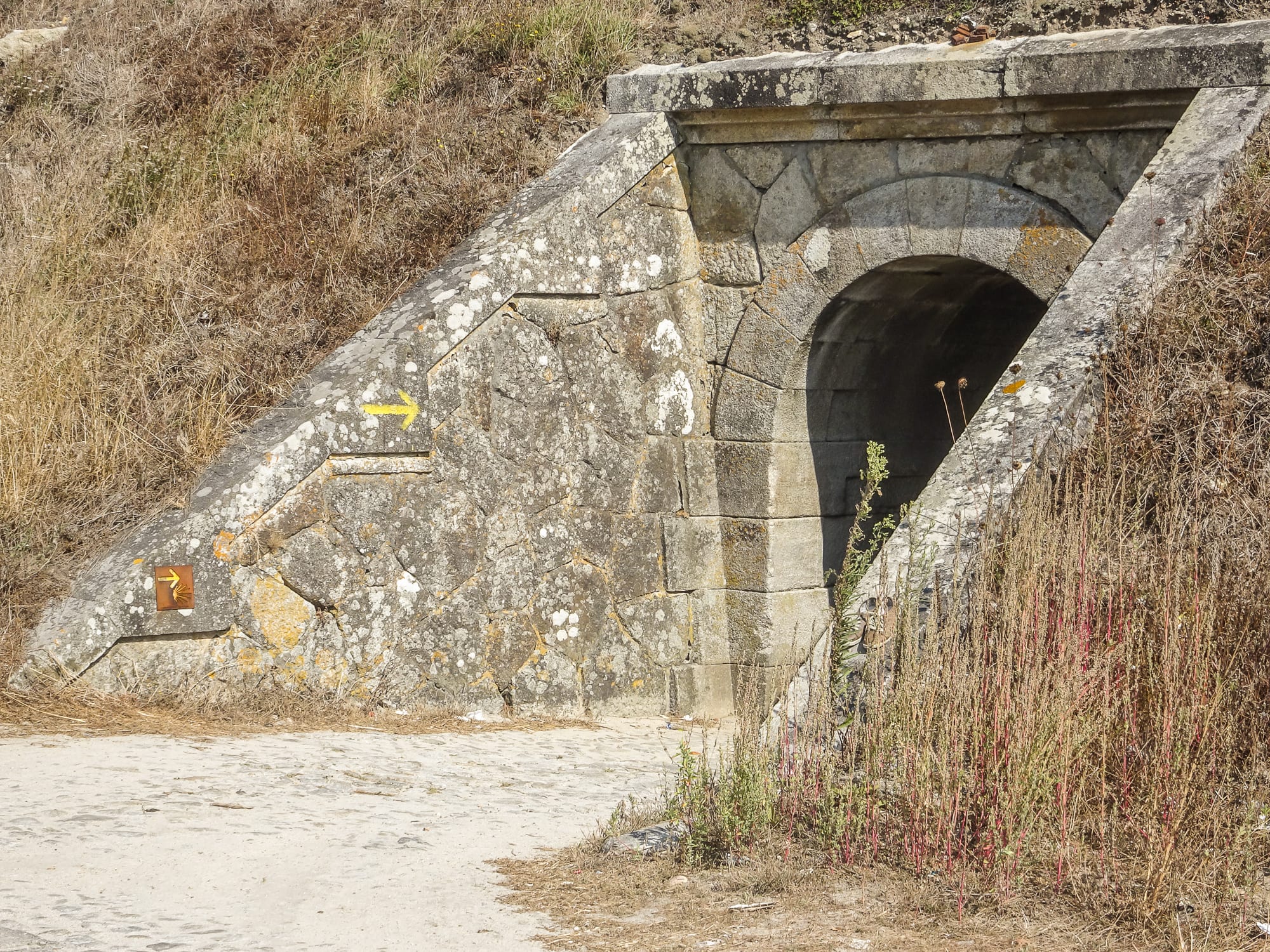 gelber Pfeil - Jakobswegmarkierung durch kleine Unterführung am Jakobsweg Portugal